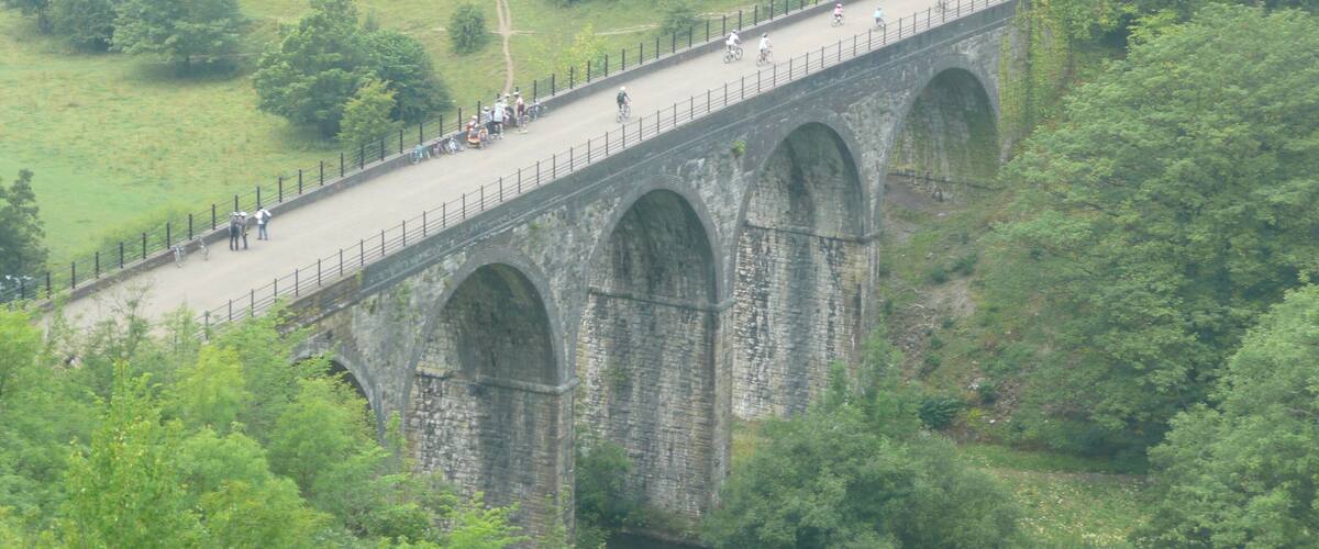 A stone bridge with multiple arches spanning a river, surrounded by lush greenery and hills.