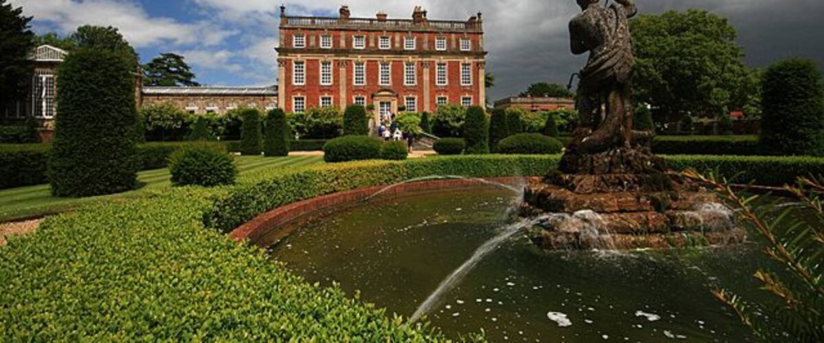 A grand building with a fountain and manicured gardens.