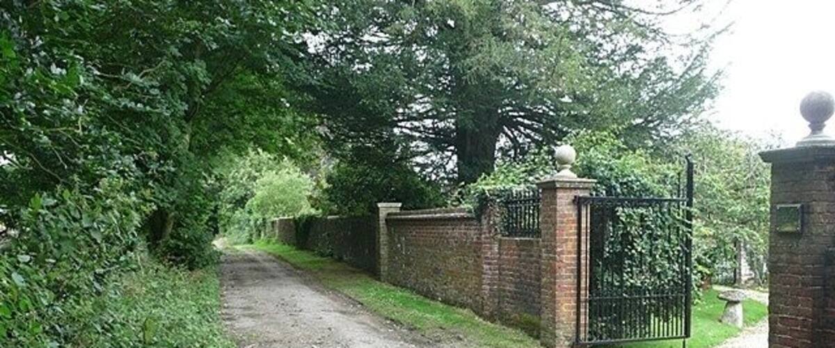 A gravel path leading to a gated entrance surrounded by lush greenery and a brick wall.