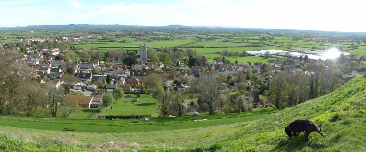 A village nestled in a valley with a prominent church tower, surrounded by green fields and hills.