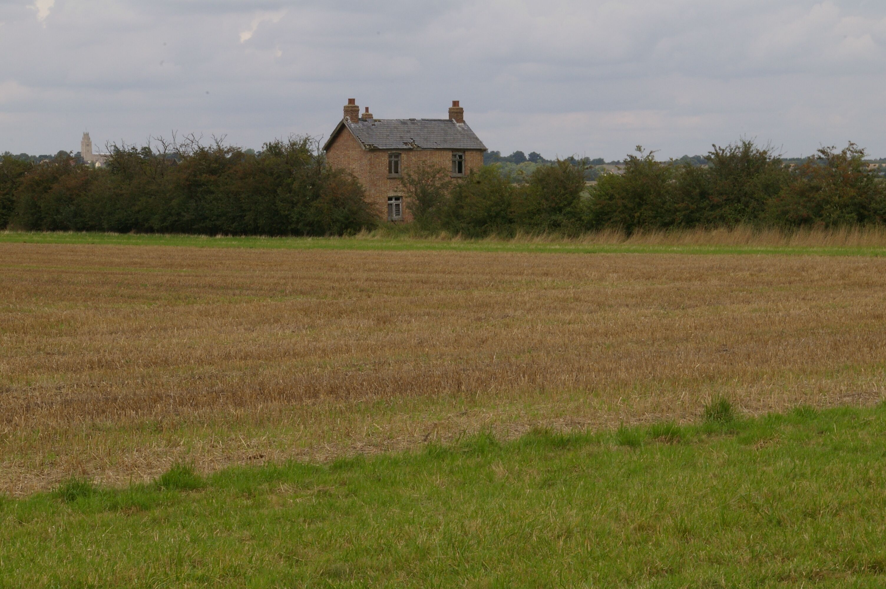 A rural landscape with a brick house surrounded by a field and dense trees.
