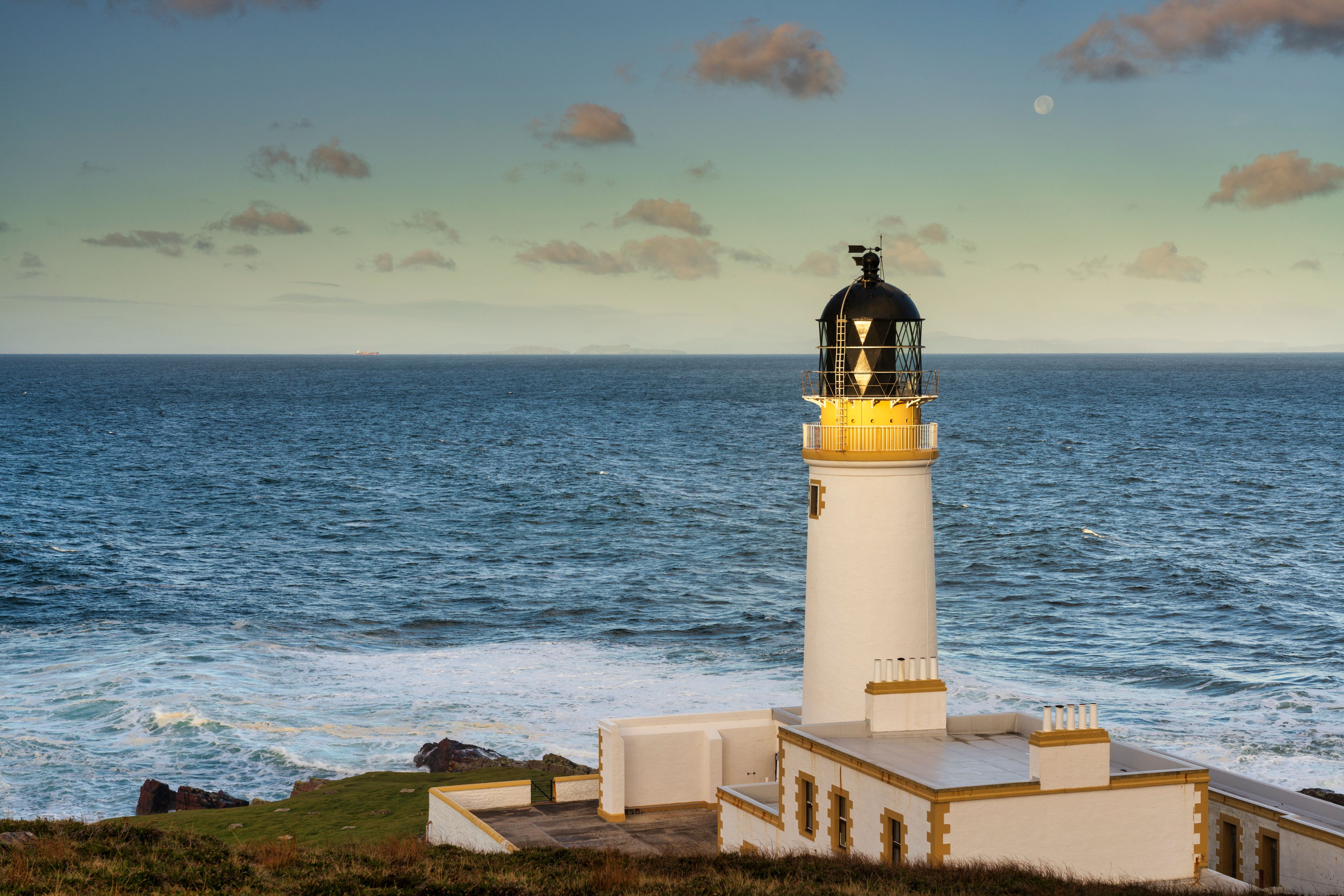 Ein Leuchtturm am Meer, Wellen schlagen an die Felsen.