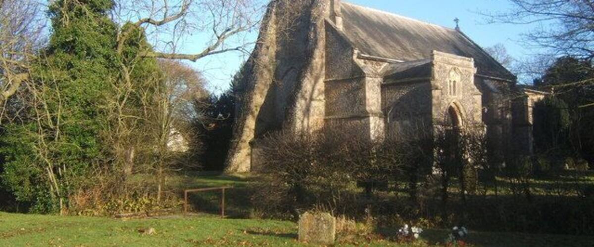 A stone church with a steeply pitched roof, surrounded by trees and a grassy area.