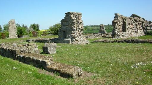 Ancient stone ruins in a grassy field with a clear sky.