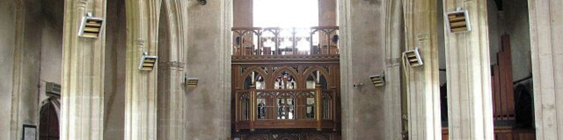 Interior de igreja com tetos abobadados, bancos de madeira e uma nave central que leva a um altar.