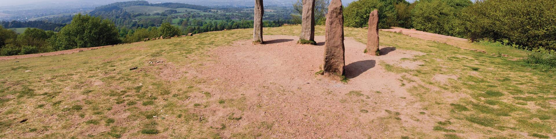 A landscape with a clear sky, a grassy hill, and several standing stones.