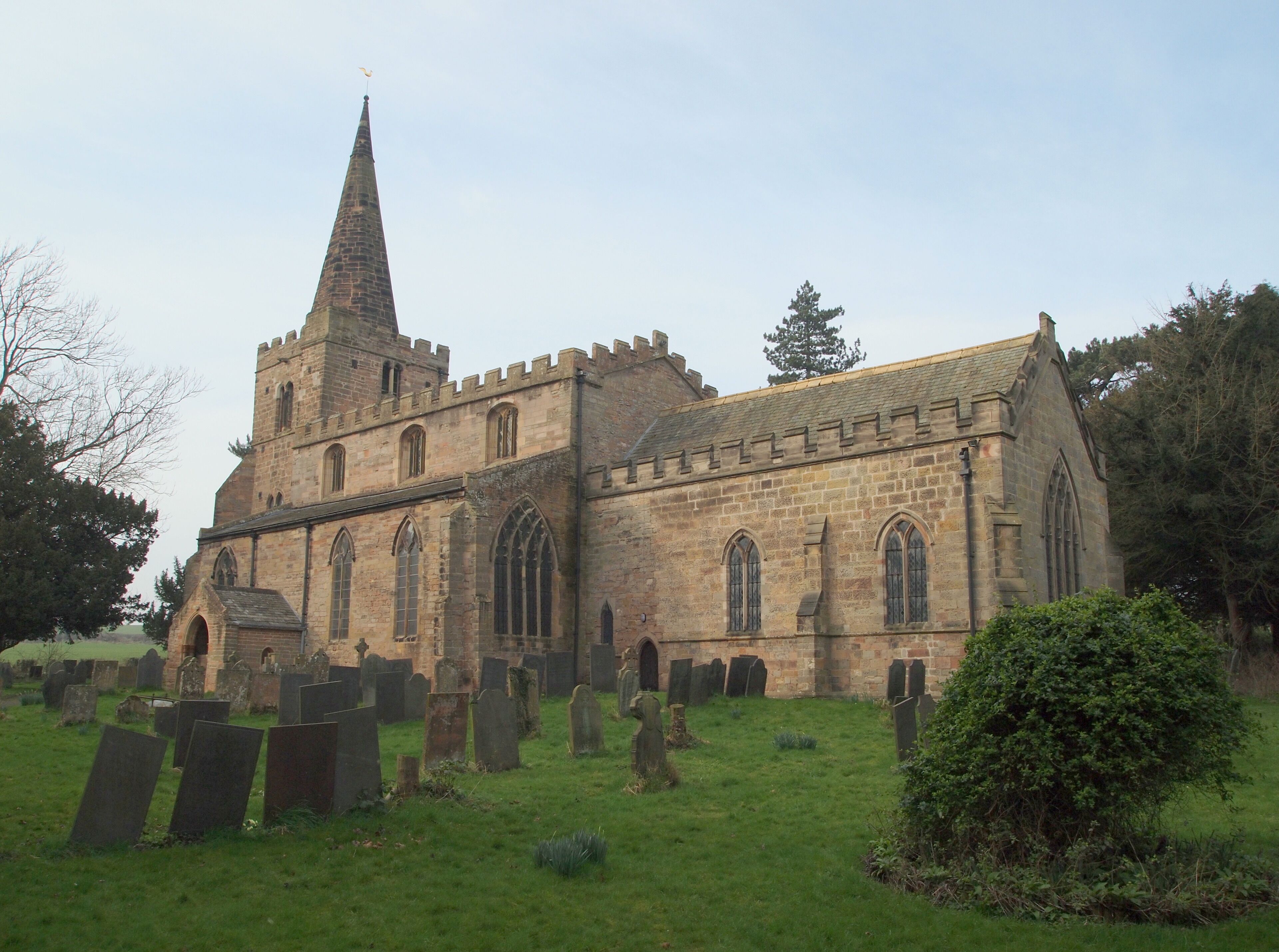 A historic church with a tall spire and a graveyard in front.