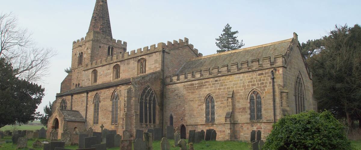 A historic church with a tall spire and a graveyard in front.