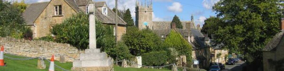 Village green, Longborough. The village green in the middle of Longborough with the war memorial in the style of a Celtic cross. In the distance the tower of St James's Church can be seen.