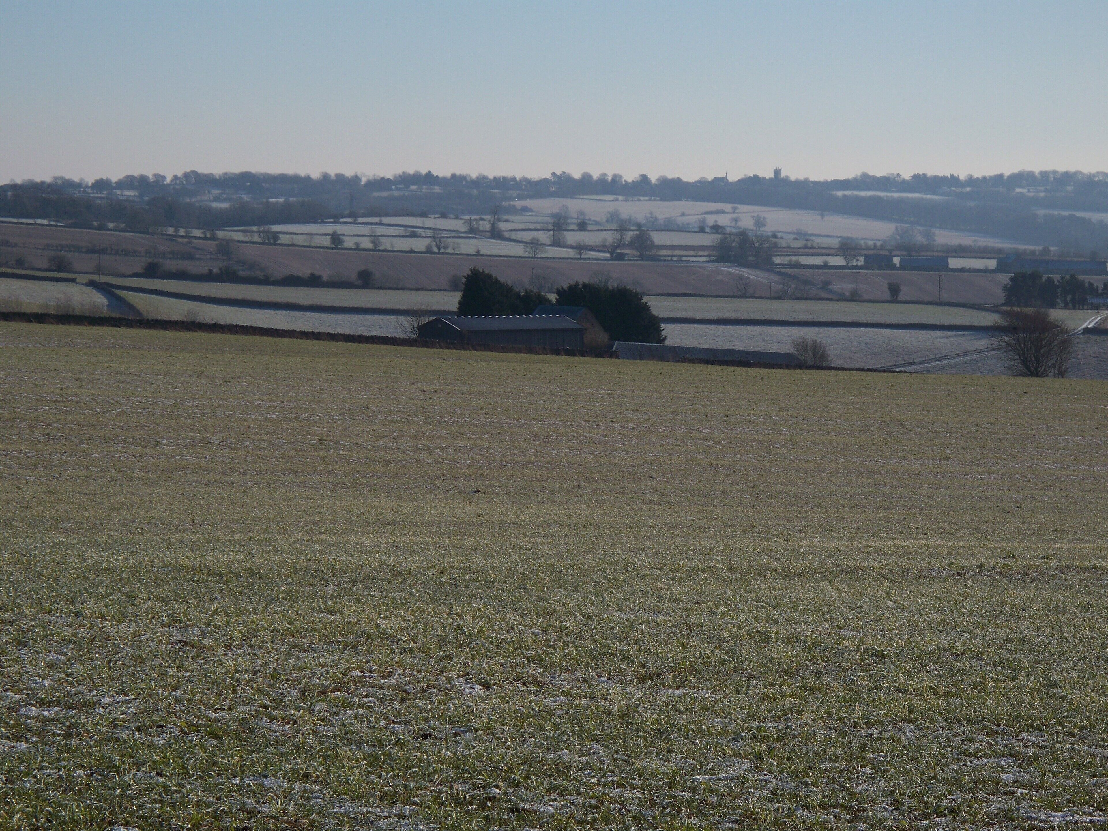 Luckley Hill Barn and view The barn is seen, across the fields, from the track. The view of the frozen landscape behind stretches all the way to Stow-on-the-Wold. The tower of Stow's parish church of St Edward is visible on the horizon to the right of the barn.