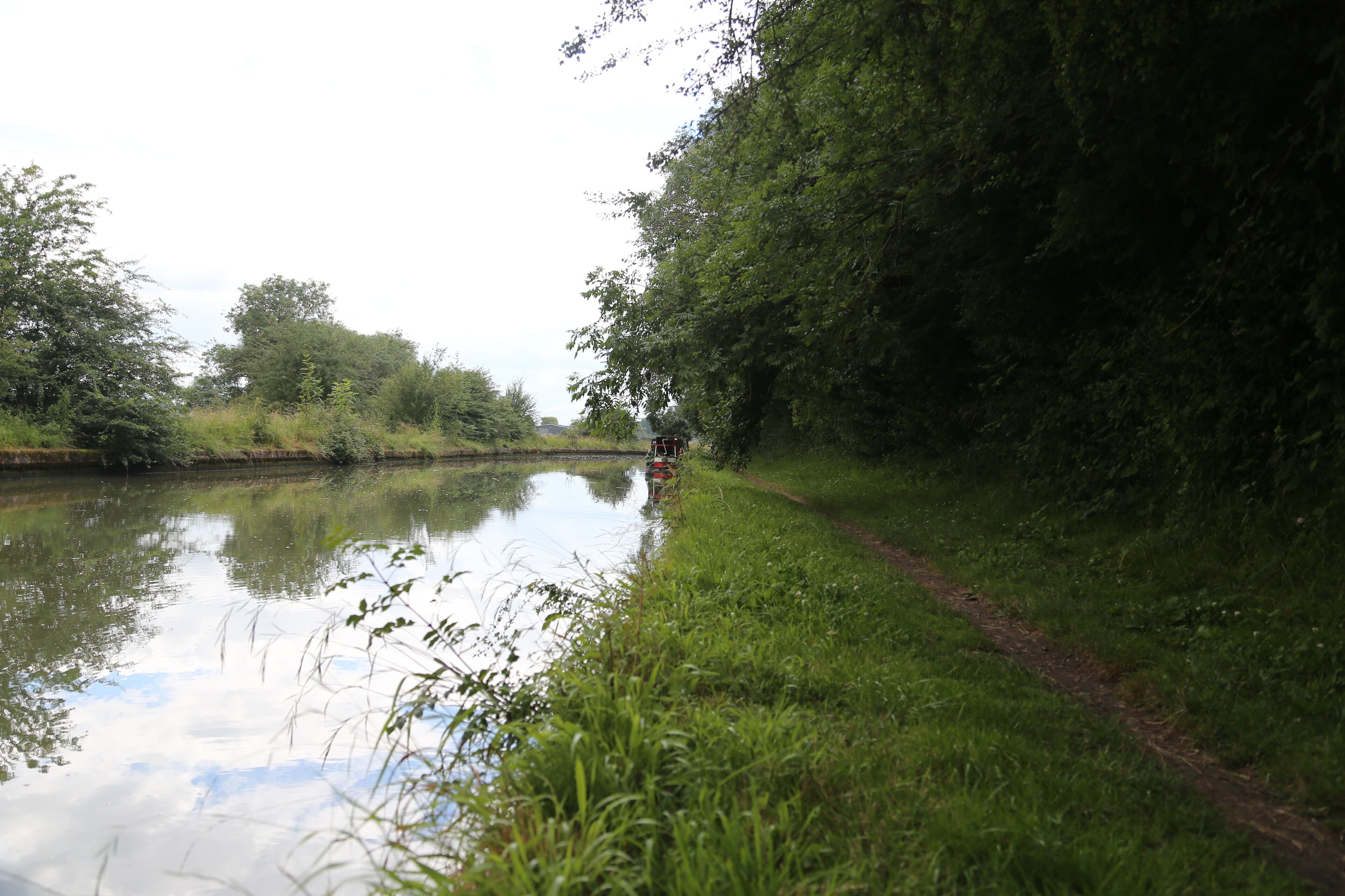 A calm river with a narrow path beside it, surrounded by lush greenery and trees.