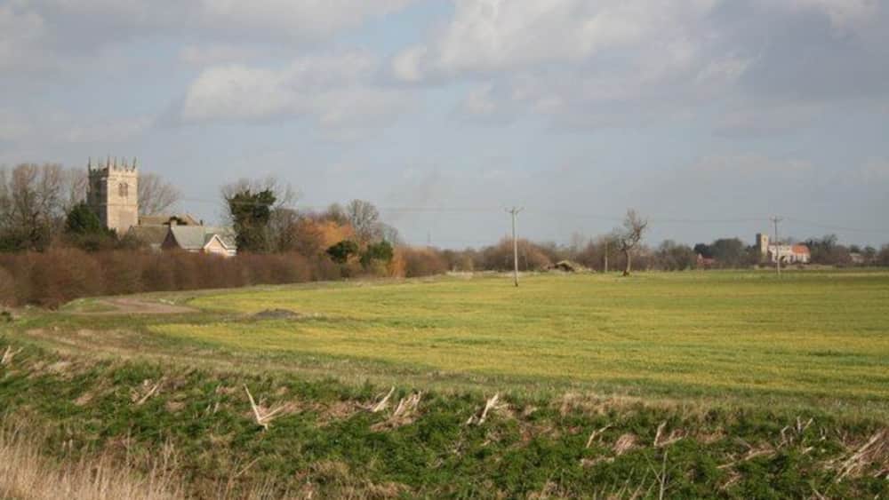 A rural landscape with a church tower, open fields, and scattered houses.