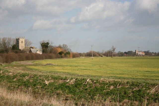 A rural landscape with a church tower, open fields, and scattered houses.