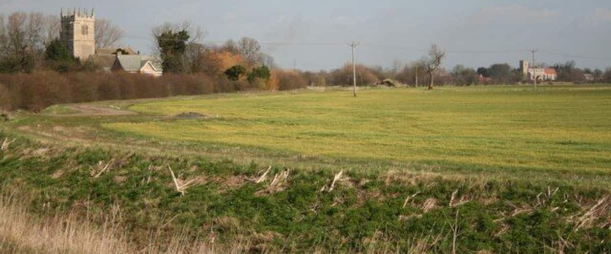 A rural landscape with a church tower, open fields, and scattered houses.