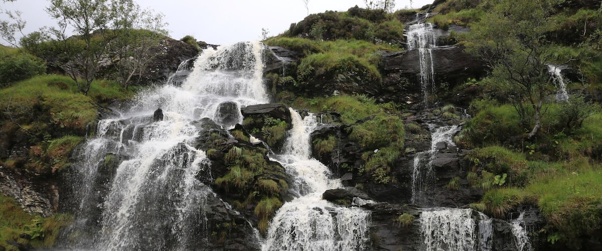 A multi-tiered waterfall cascading over rocky terrain surrounded by lush greenery.