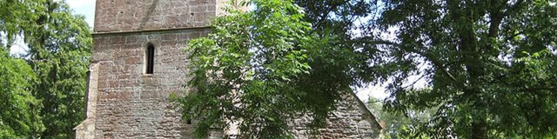 Ruined church of St John the Baptist, near to Llanwarne, Herefordshire, Great Britain. Viewed from the west this shows the tower (with columbarium), south aisle and porch. Abandoned in 1864 due to constant flooding from the nearby Gamber Brook, the roofless church is now in a fairly dangerous condition. Across the road, and built on higher ground, is Christ Church where some artefacts from St John the Baptist's, including an ancient font, have been re-housed.