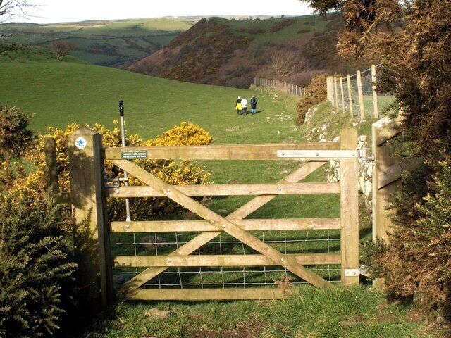 A wooden gate with a sign, a grassy field, and a hilly landscape in the background.