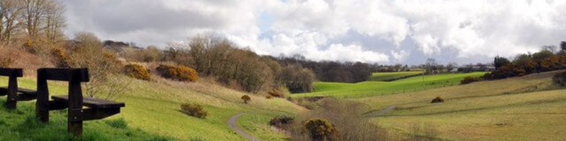 A grassy path, a wooden bench, and rolling hills in the background.