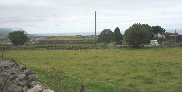 A rural landscape with a stone wall, a fence, and a distant view of houses and trees.