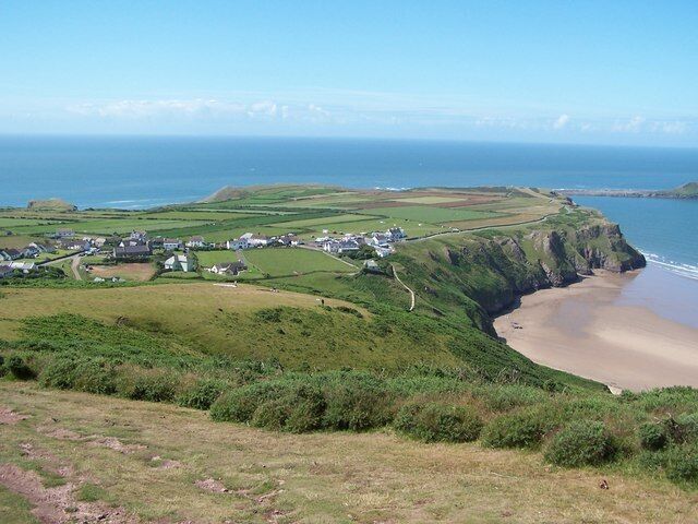 A coastal landscape with a beach, grassy hills, and a small settlement.