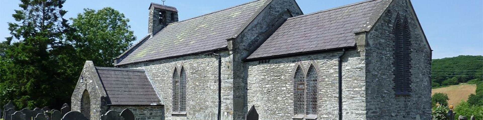 A stone church with a steeple and a graveyard with headstones.