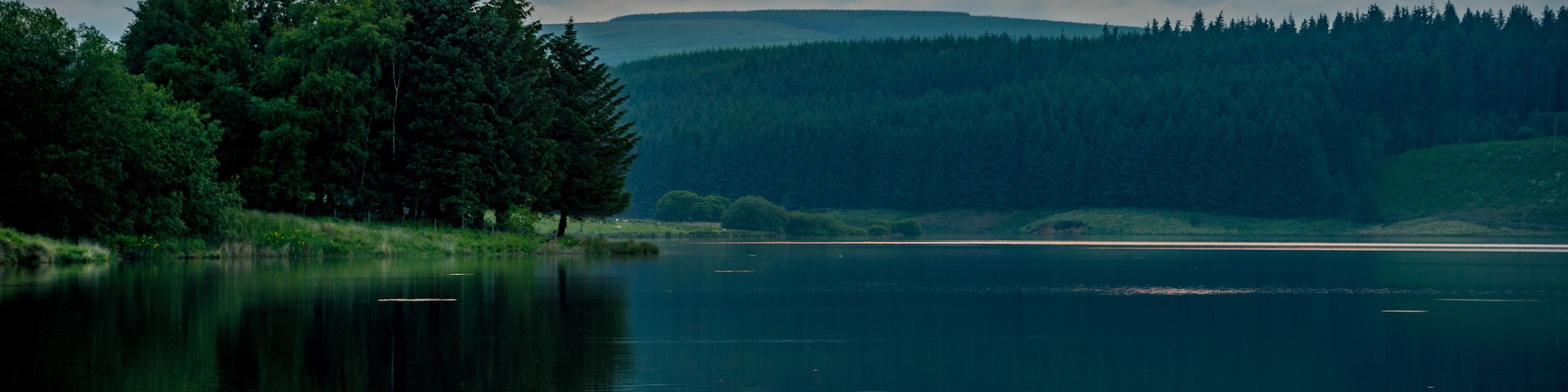 Un lac paisible où se reflète le coucher de soleil, entouré d’une forêt dense et de collines.