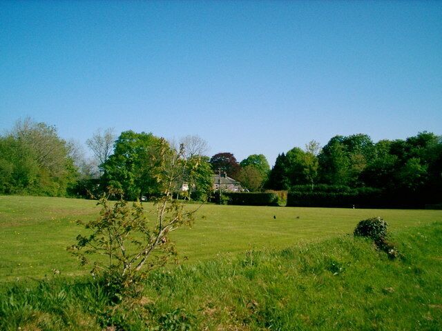 A grassy field with a building in the distance, surrounded by trees.