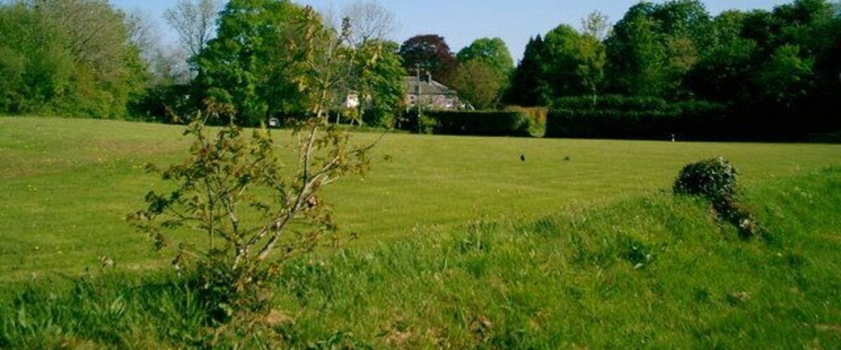 A grassy field with a building in the distance, surrounded by trees.