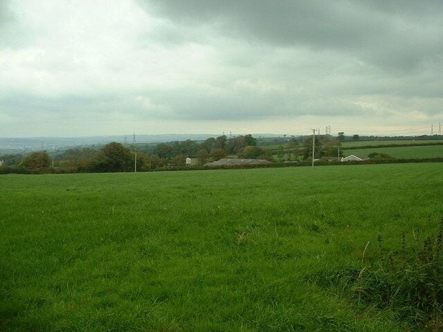 A green field with a cloudy sky and distant buildings.