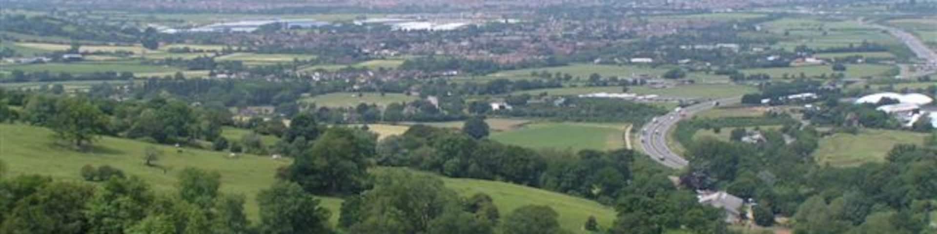 A green valley with a winding road, trees, and distant buildings.