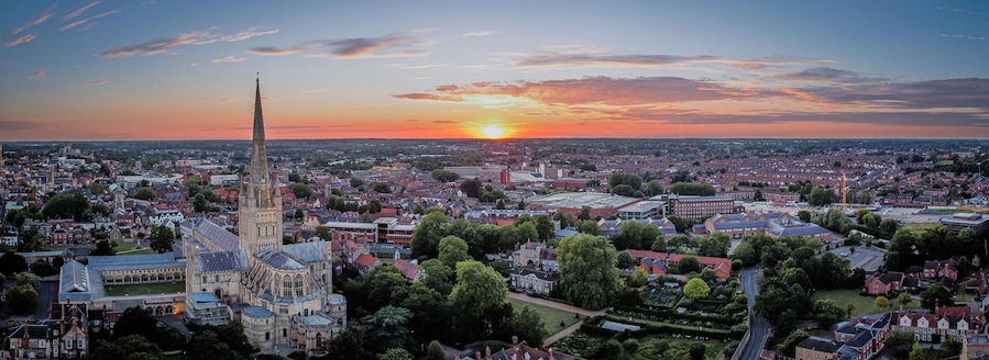 Un paisaje urbano al atardecer con una destacada aguja de iglesia y un edificio grande con una torre de reloj.