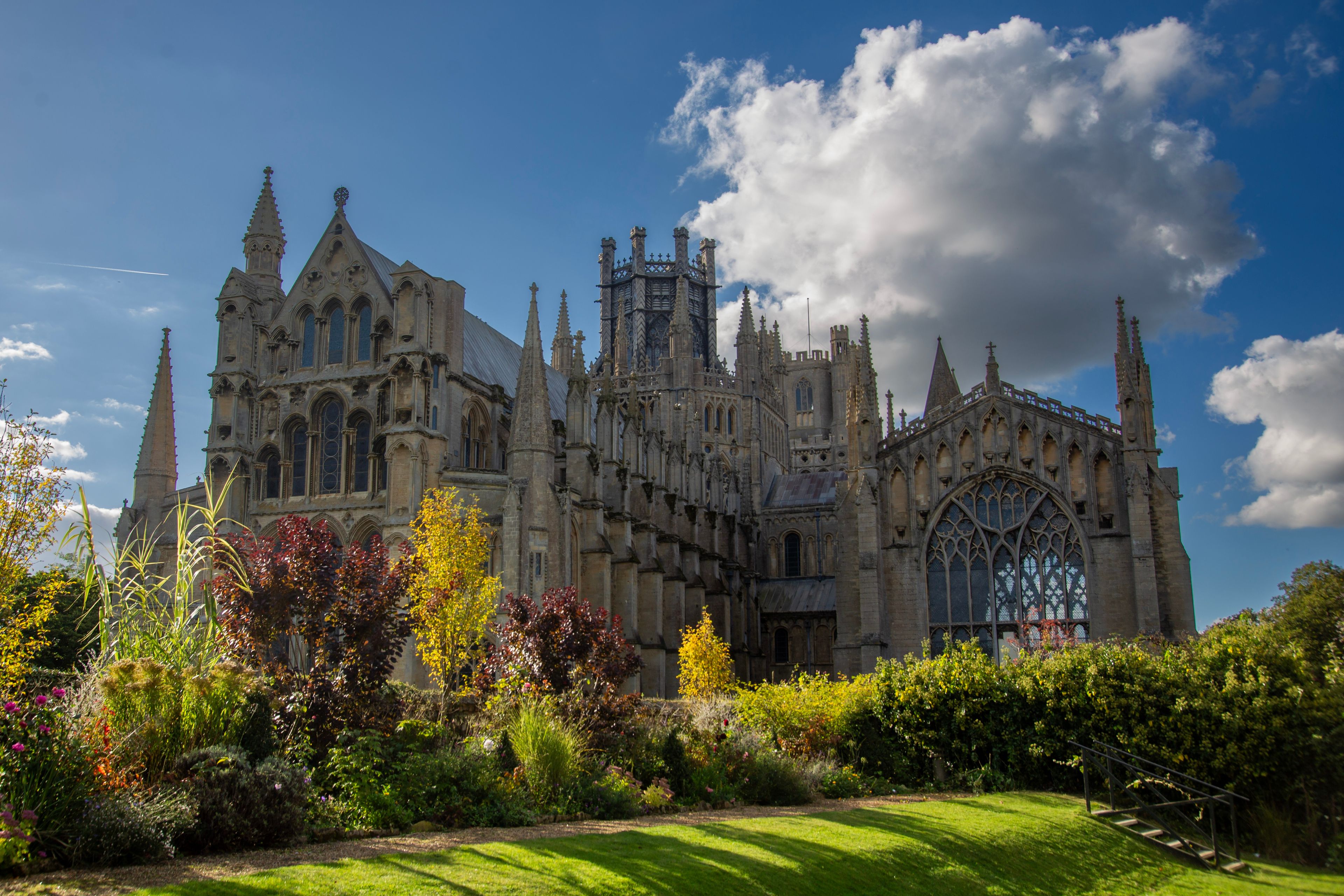 A historic cathedral with intricate Gothic architecture, surrounded by lush gardens and a clear blue sky.