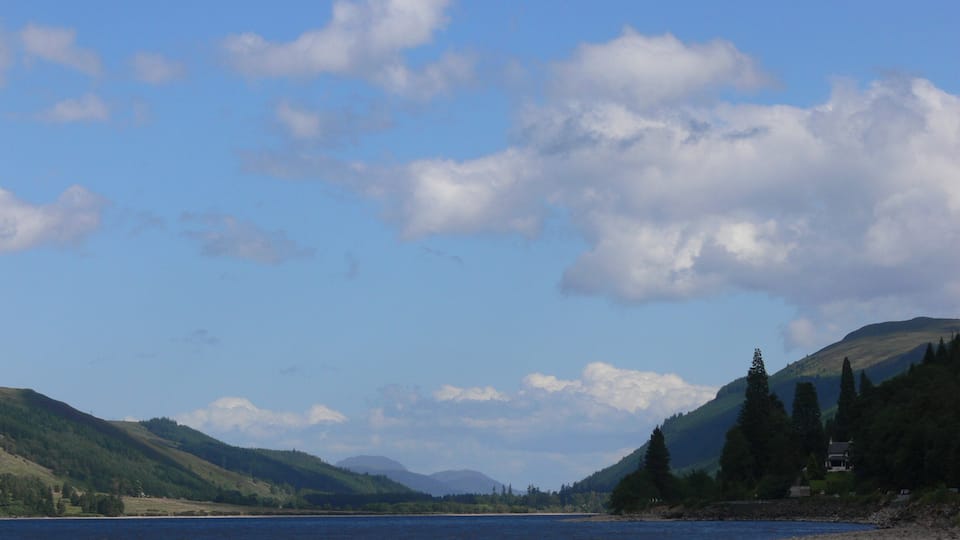 A calm lake with mountains in the background and a clear sky.