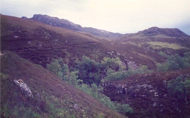A rugged mountainous landscape with dense green vegetation and rocky terrain.