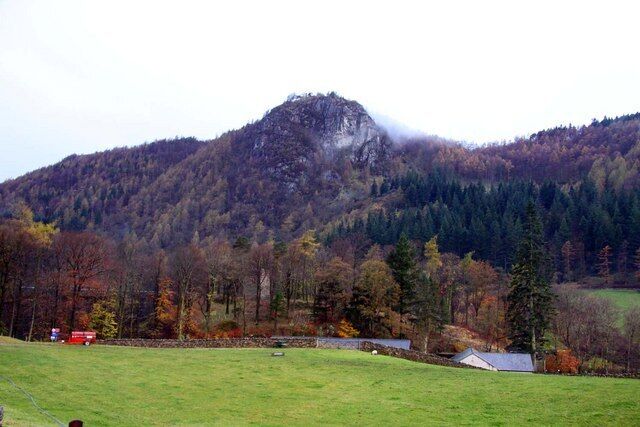 A mountainous landscape with a grassy field, a stone wall, and a small building.