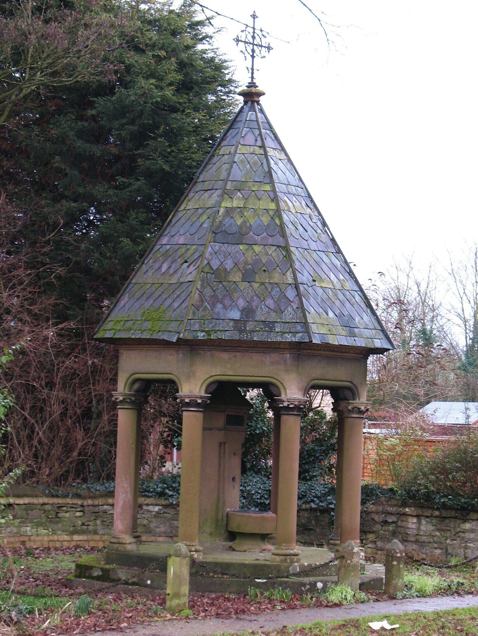 A stone gazebo with a pointed roof and a weather vane atop.