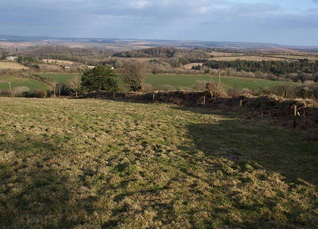 A rural landscape with rolling fields, a stone wall, and distant hills.