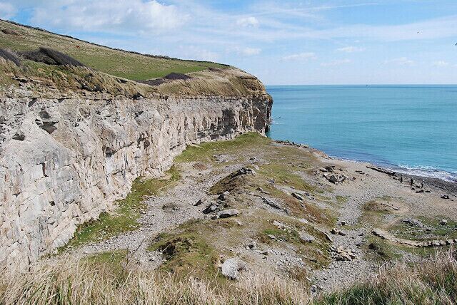 A coastal cliff with a grassy top and a rocky base.