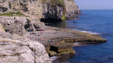 A rocky coastline with people sunbathing and swimming.