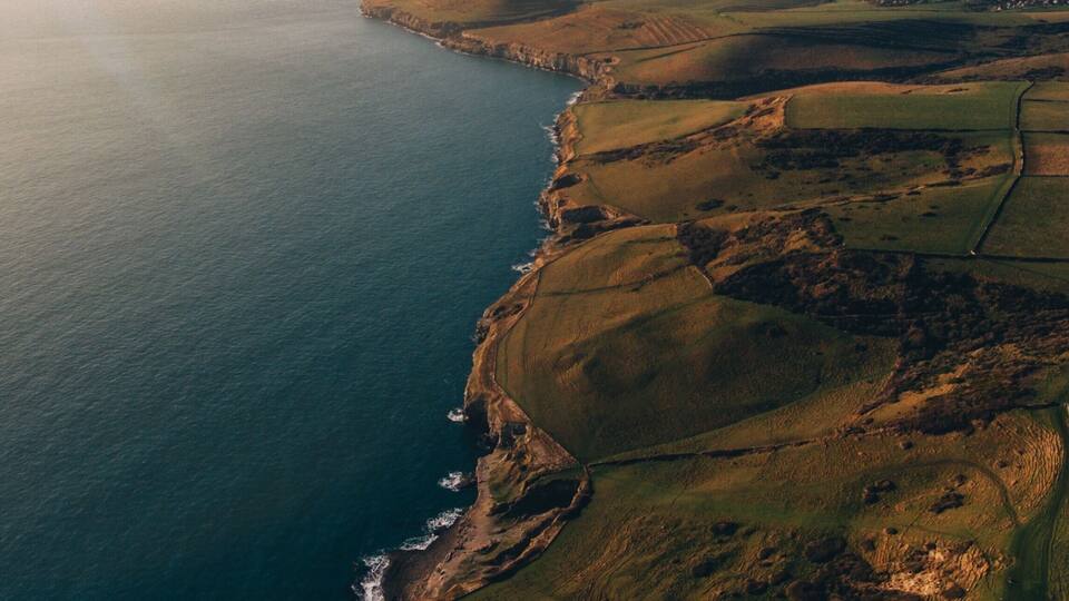 An aerial view of a coastal landscape with fields, cliffs, and a small settlement by the sea.