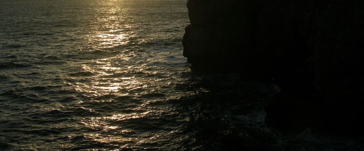 A sunset over the ocean with a rocky cliff.