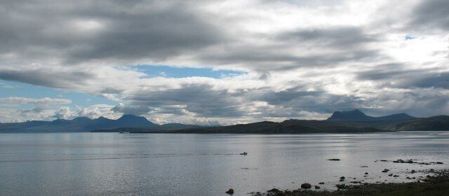 A calm lake with mountains in the background and a cloudy sky.