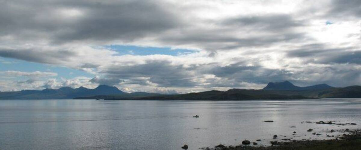 A calm lake with mountains in the background and a cloudy sky.