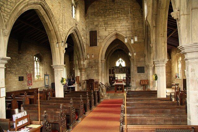 An interior of a church with stone arches, wooden pews, and a red carpet leading to the altar.