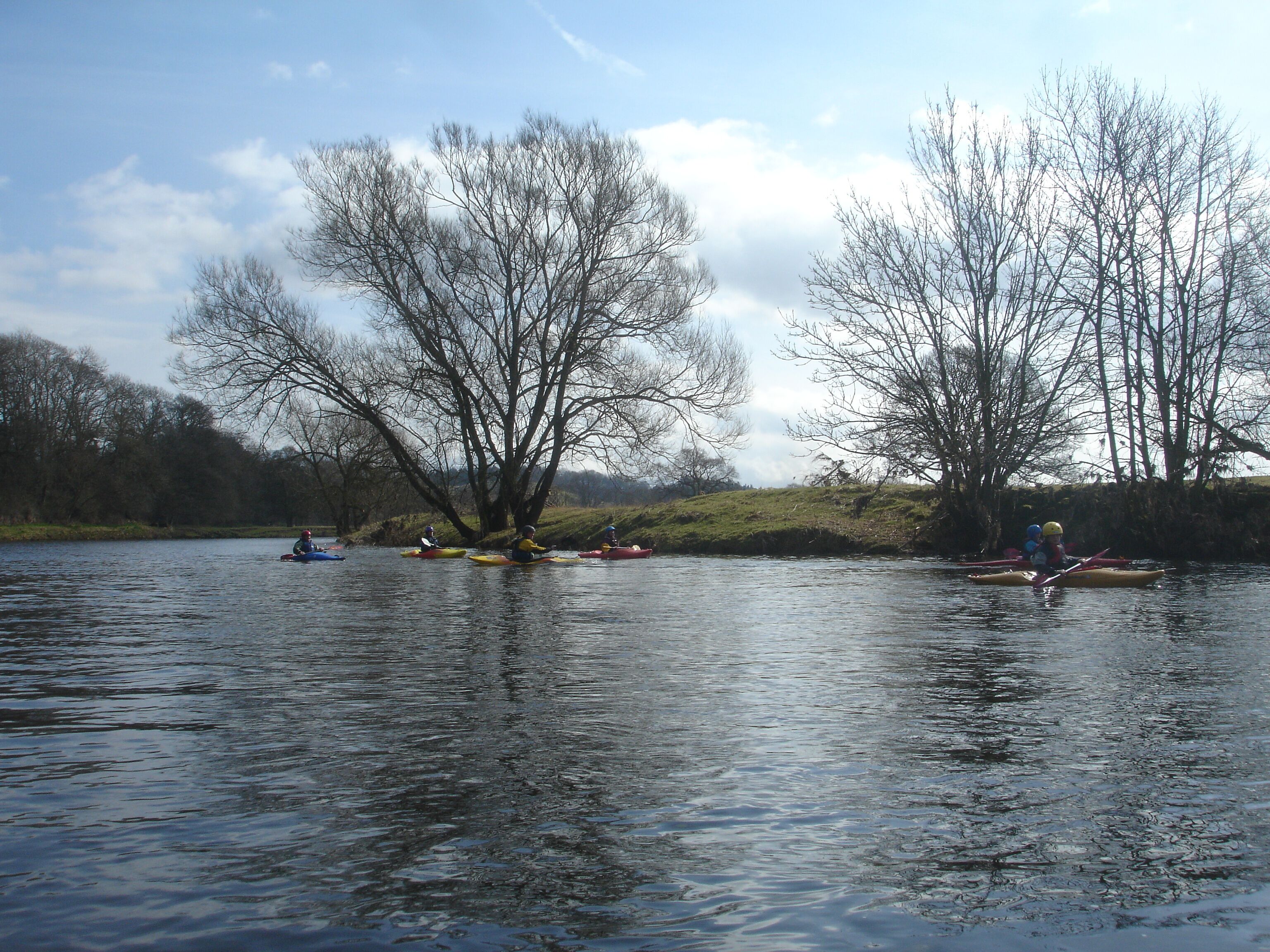 A calm river with kayakers in various colors.