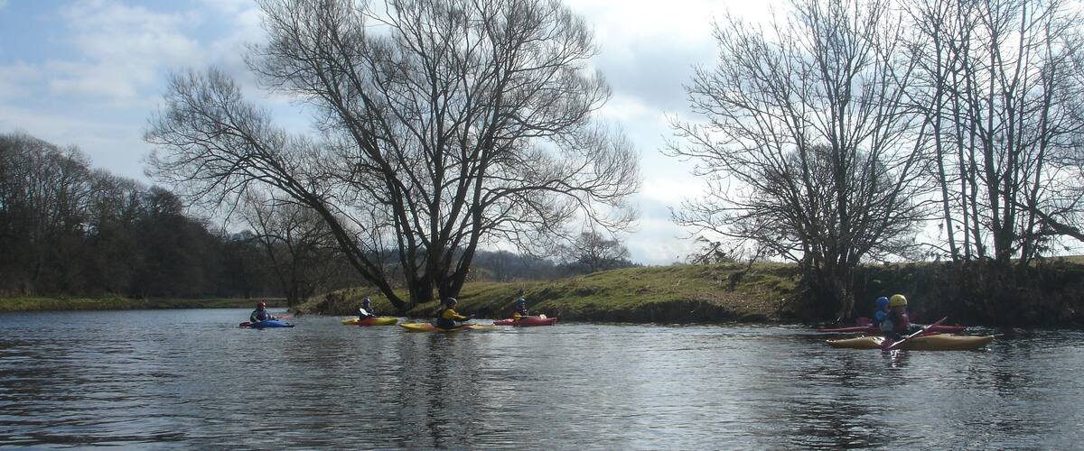A calm river with kayakers in various colors.