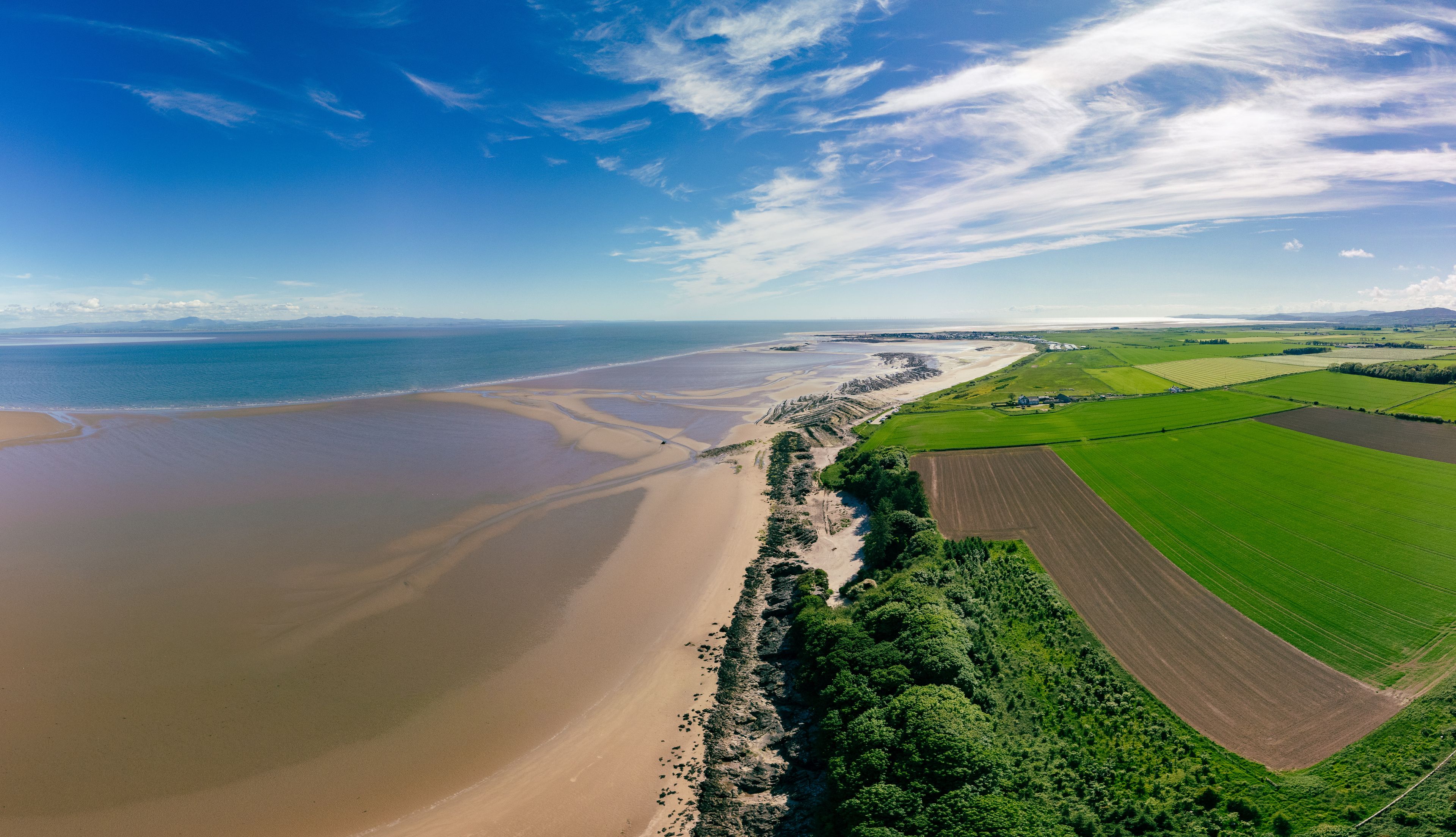 Paesaggio costiero con spiaggia sabbiosa, campi verdi e cielo azzurro limpido.