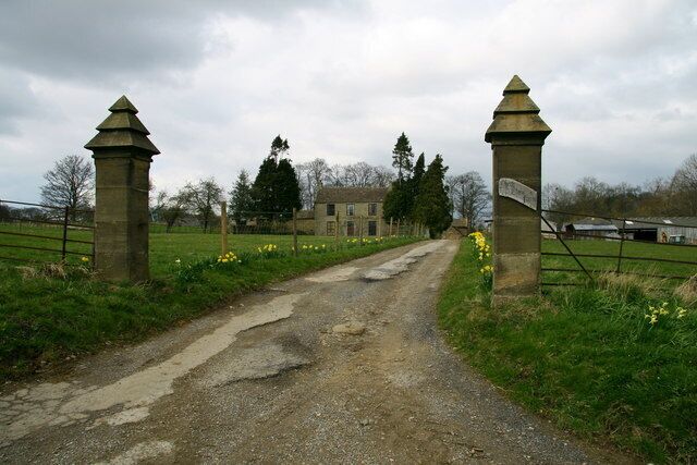 A gravel path leading to a stone gate with a building in the background.