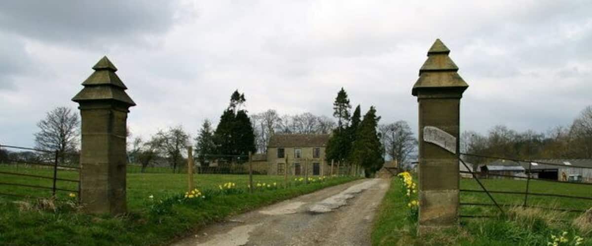A gravel path leading to a stone gate with a building in the background.
