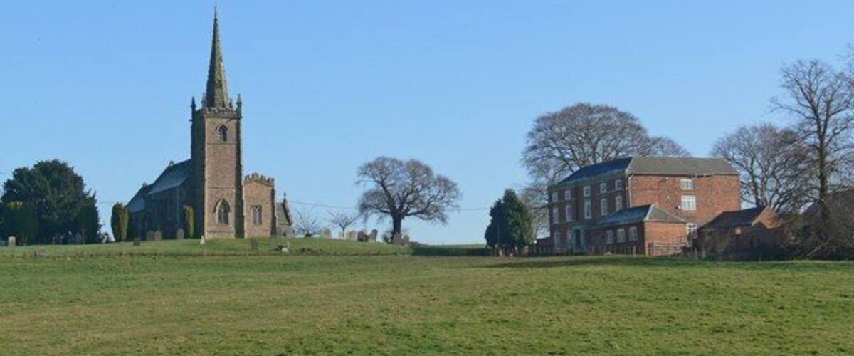 A church with a tall spire, a brick building, and a grassy field.